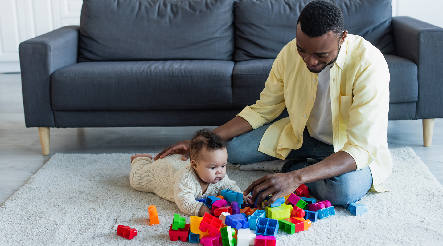 dad playing with baby on tummy and colorful blocks