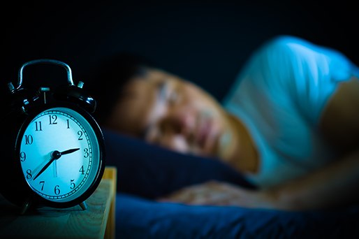 clock in foreground man sleeping in bed in dark room