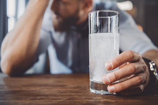 man with hangover holding glass of fizzy water