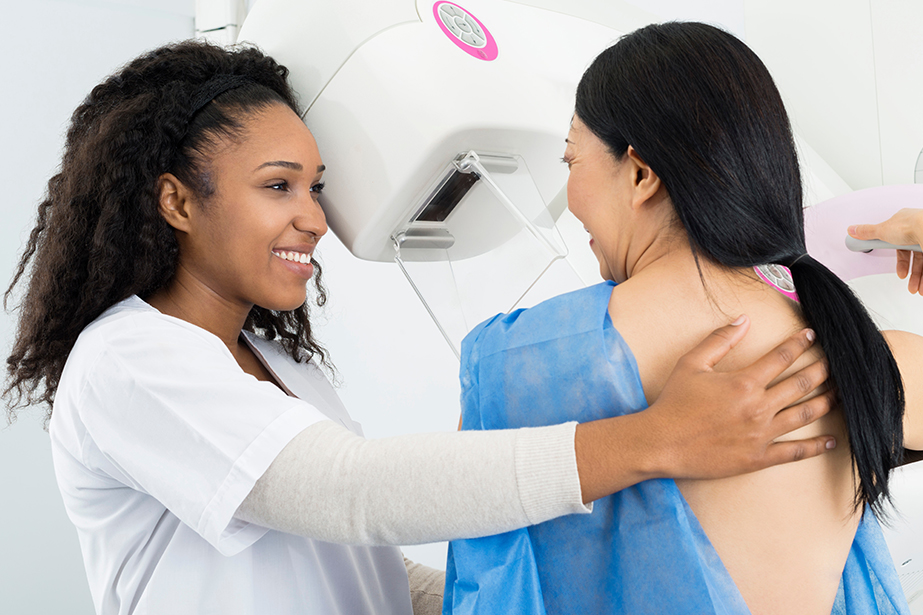 mammography technician touching woman's back during mammogram